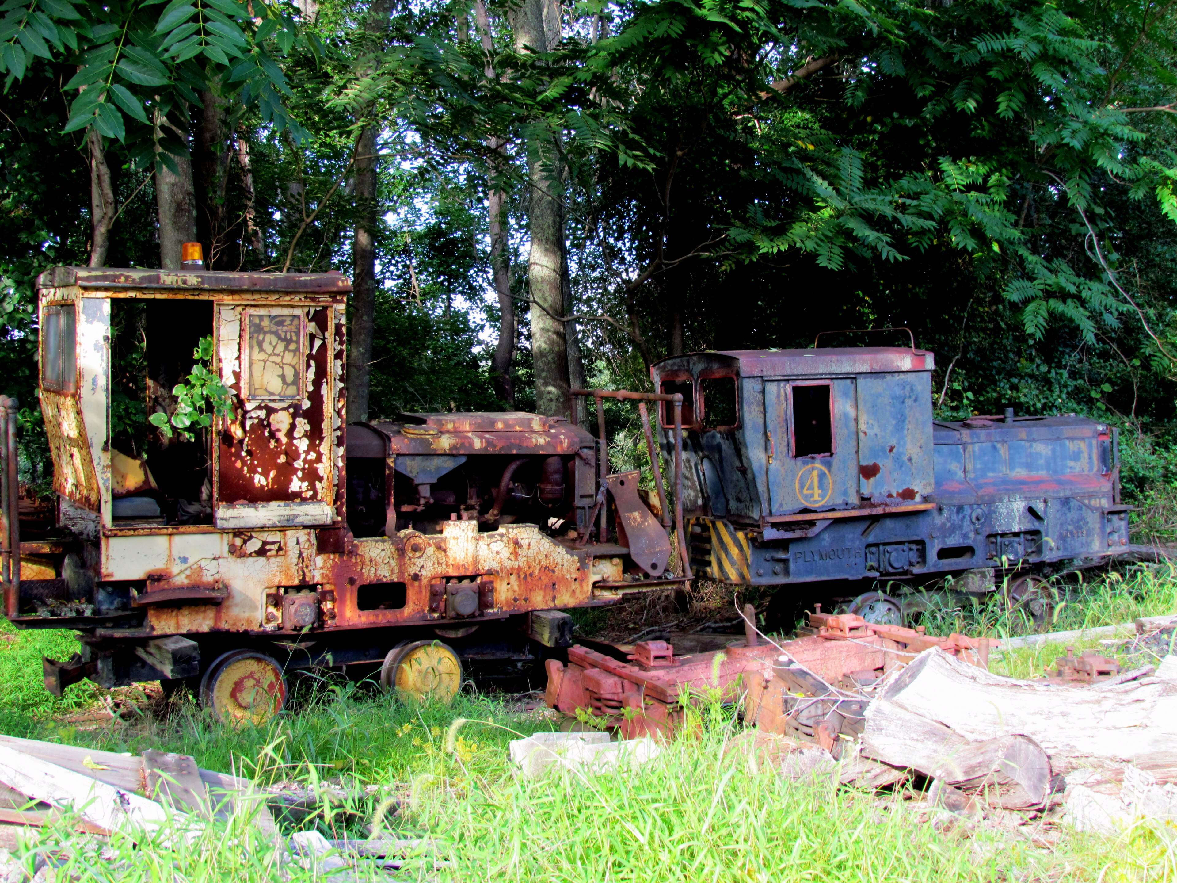 Rusted industrial locomotives and equipment sitting in the grass beneath trees at Allaire State Park.