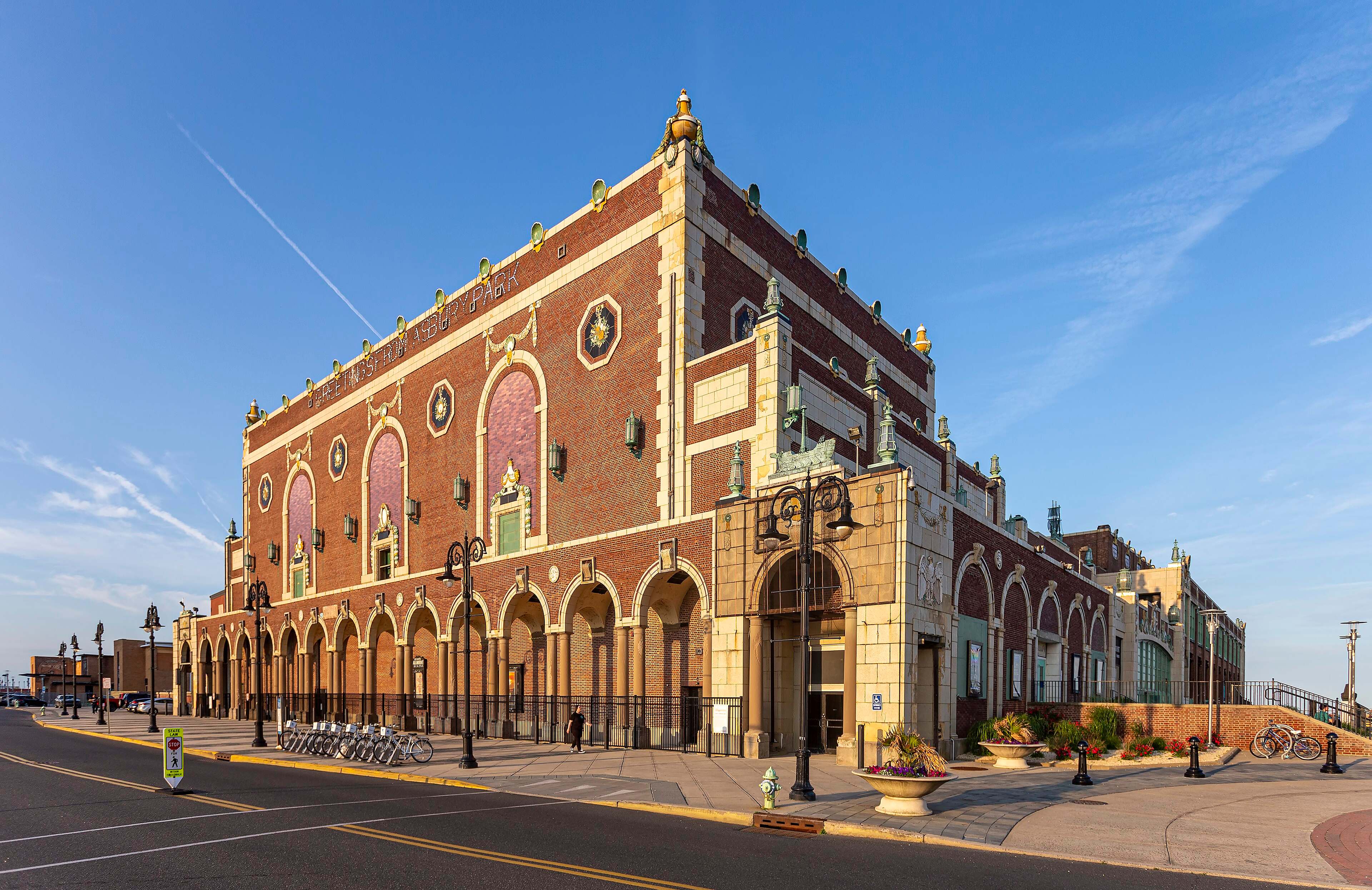 Red-brick Asbury Park Convention Hall with arched windows and ornate trim, seen from the street in late-day light.