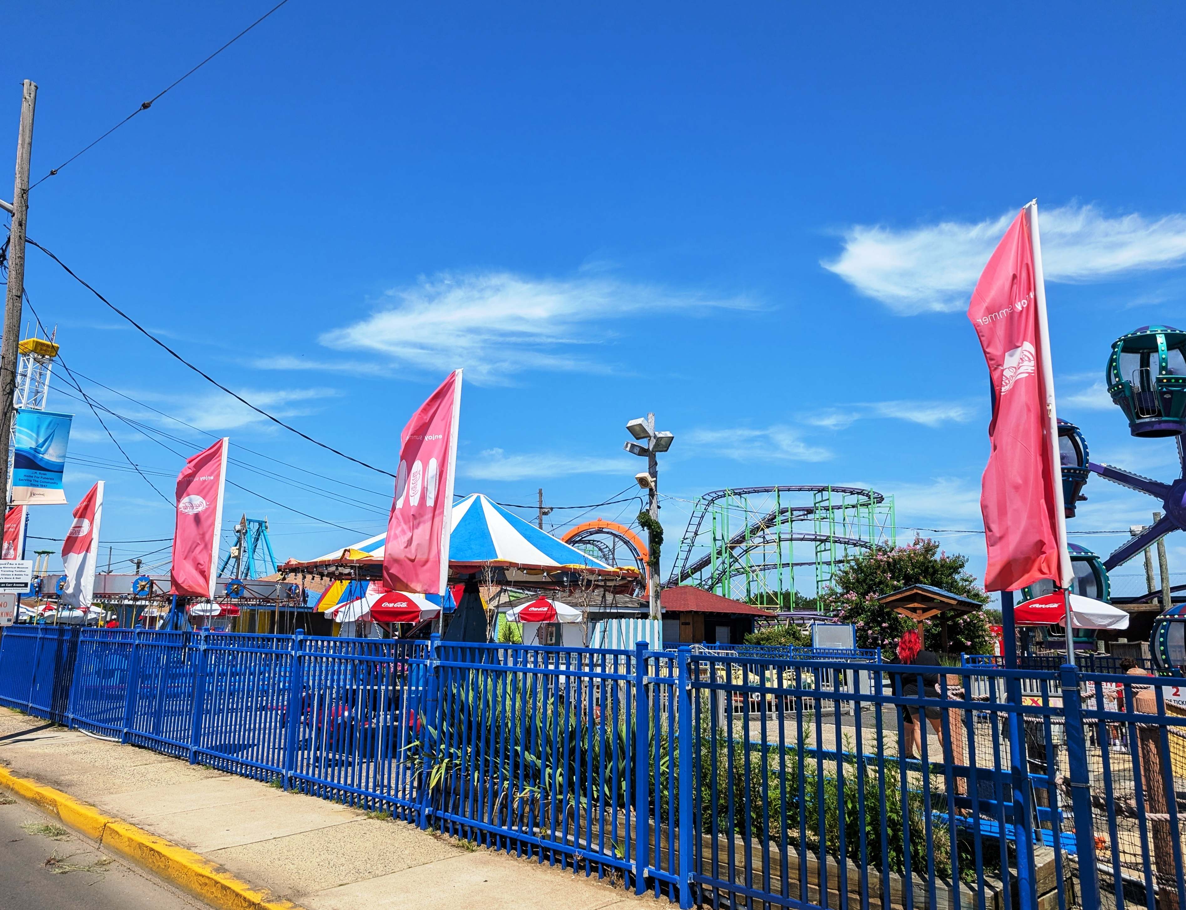 Bright pennant flags above a blue fence at Keansburg Amusement Park, with rides and a roller coaster beyond.