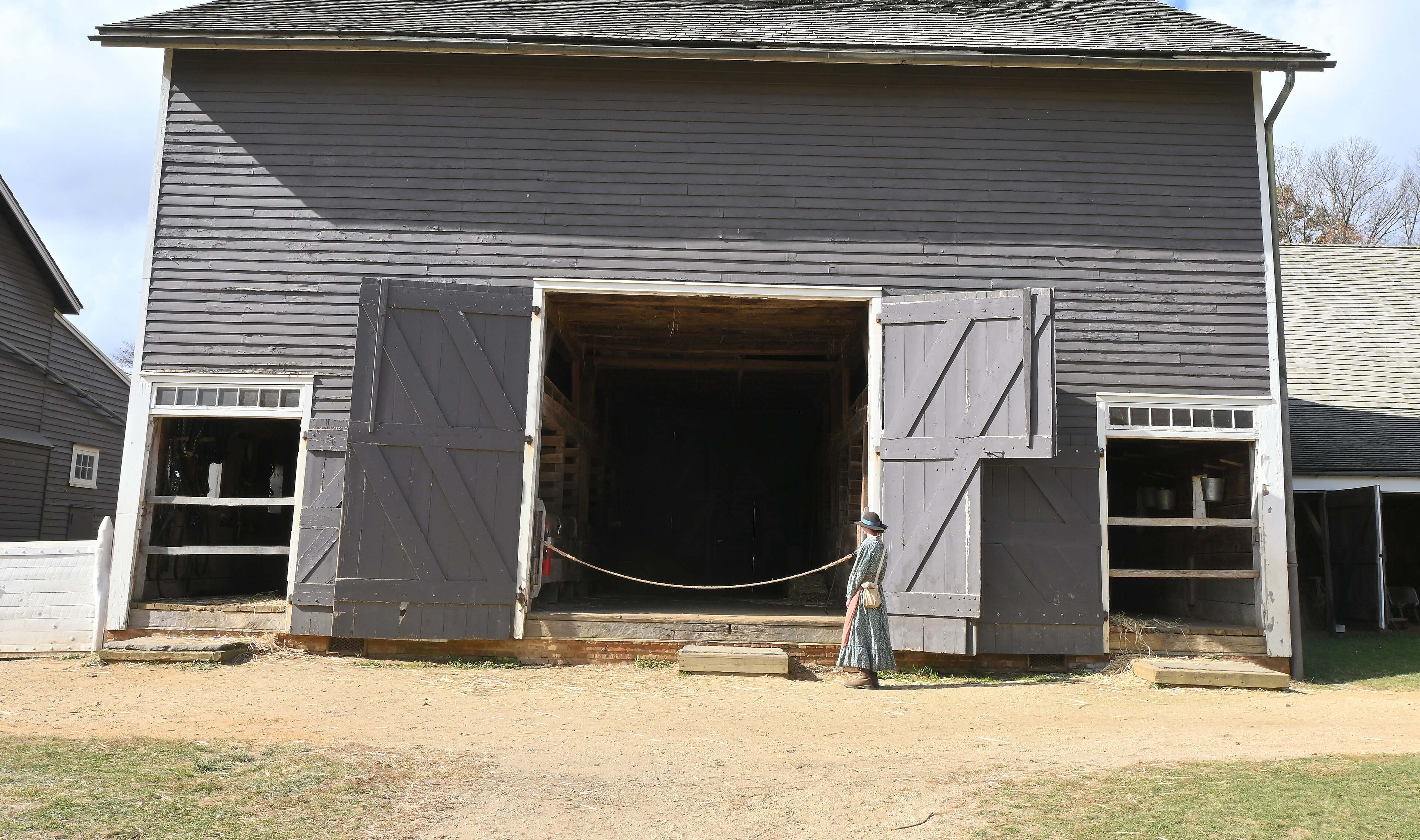 The gray barn at Longstreet Farm in Holmdel with its doors open and a person in period dress at the entrance.