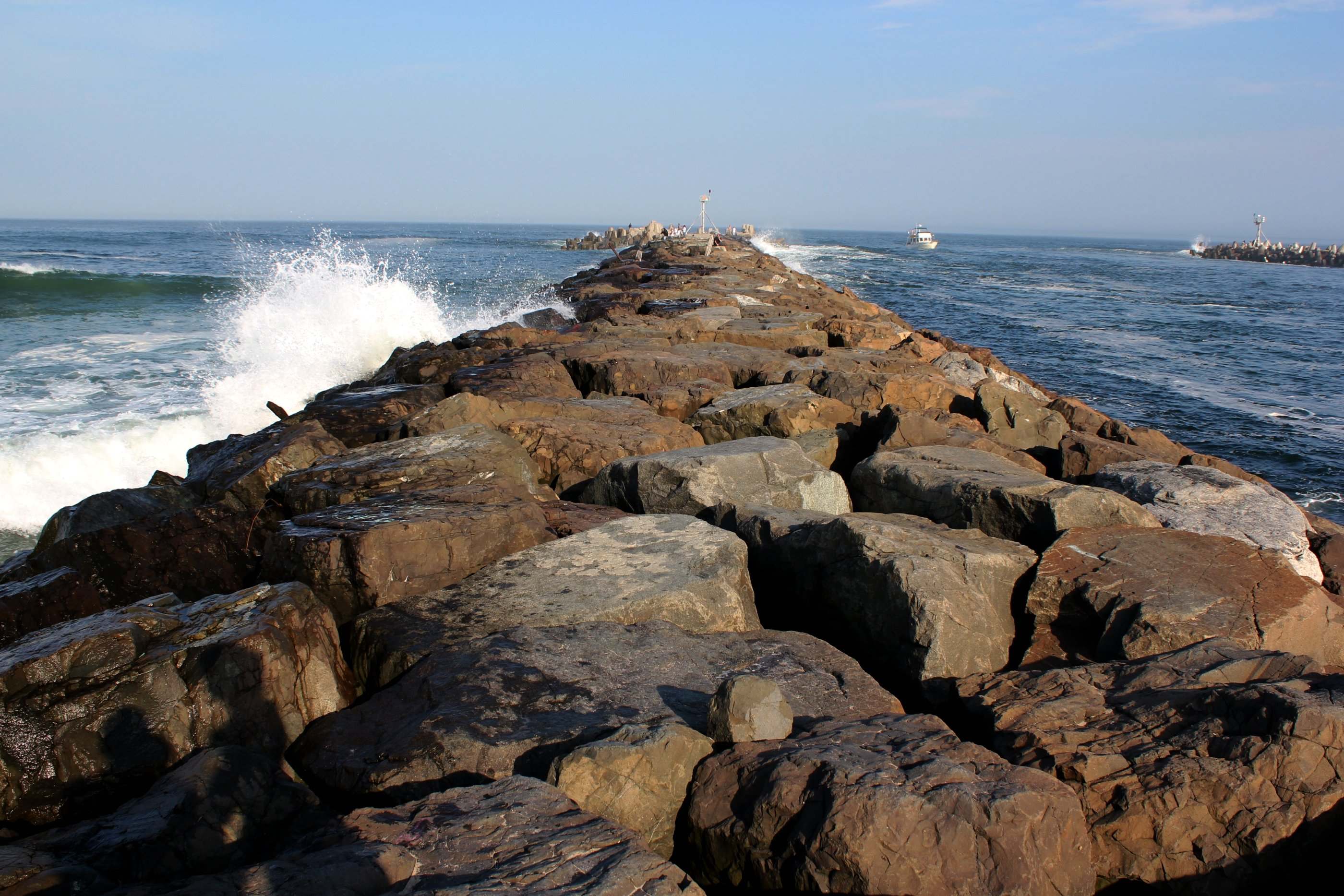 Granite boulders of the Manasquan Inlet jetty running out to sea as a wave breaks on the left.