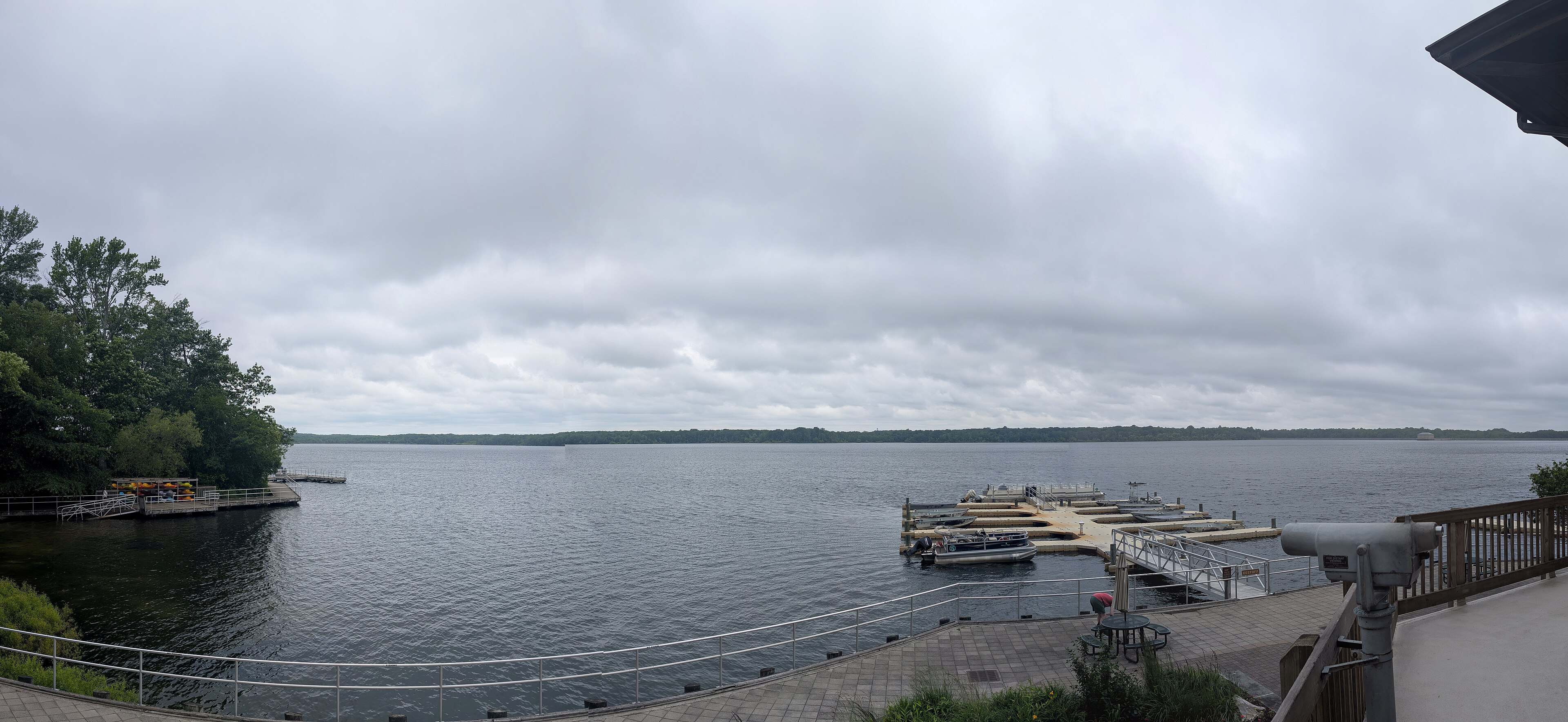 Boat docks and a railed waterfront terrace on Manasquan Reservoir under an overcast sky.